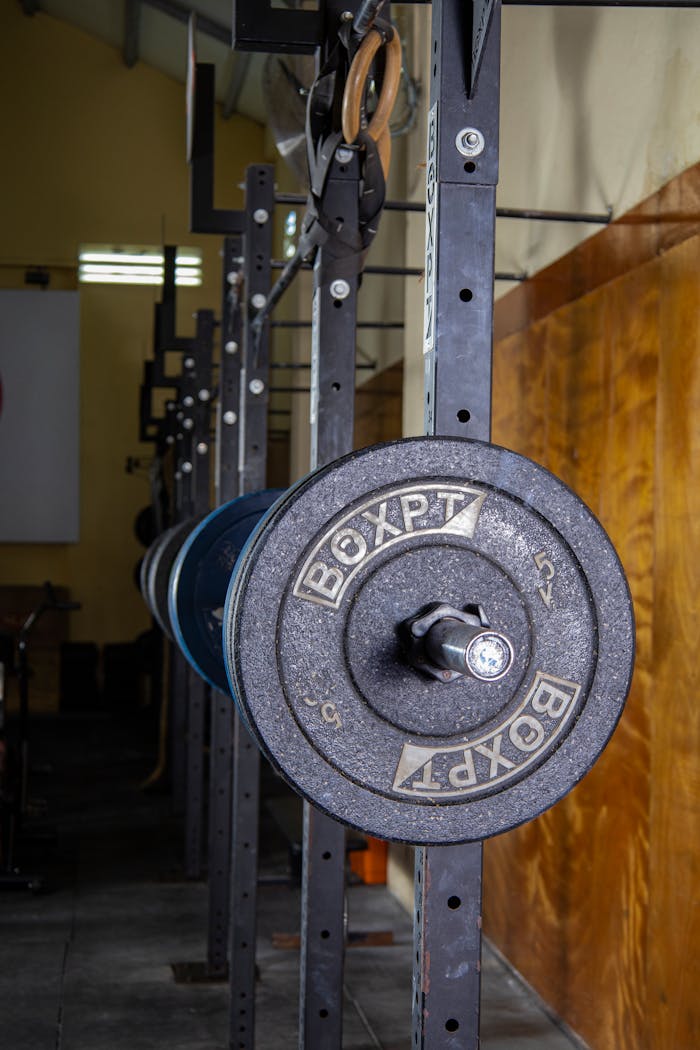 Close-up of a barbell setup in a gym with equipment and industrial lighting.