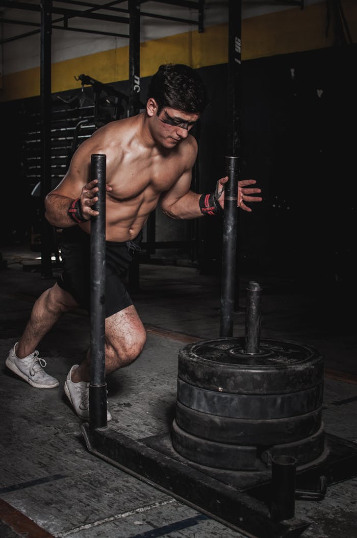 A muscular man pushes a weighted sled in an indoor gym, showcasing strength and endurance.