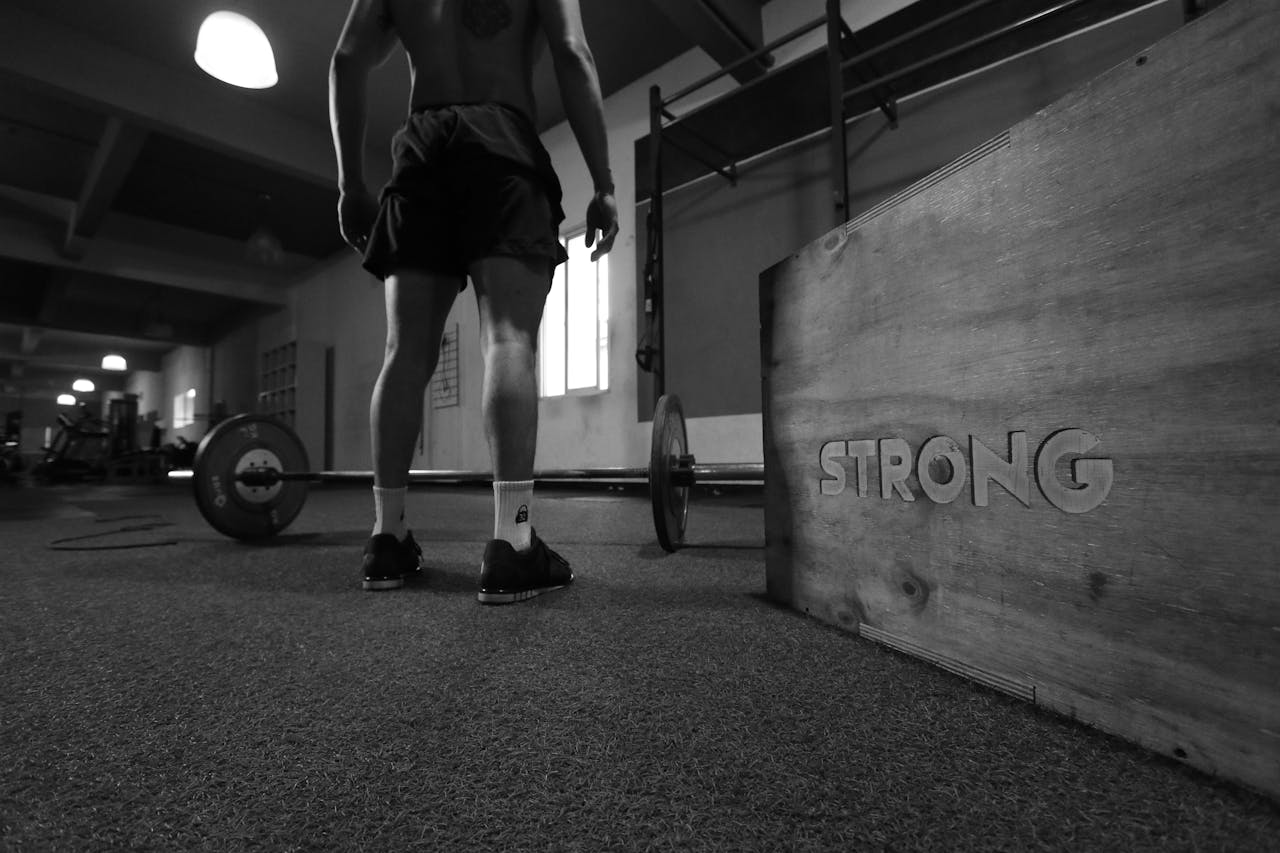 Black and white photo of a man in a gym with barbell and 'Strong' box.