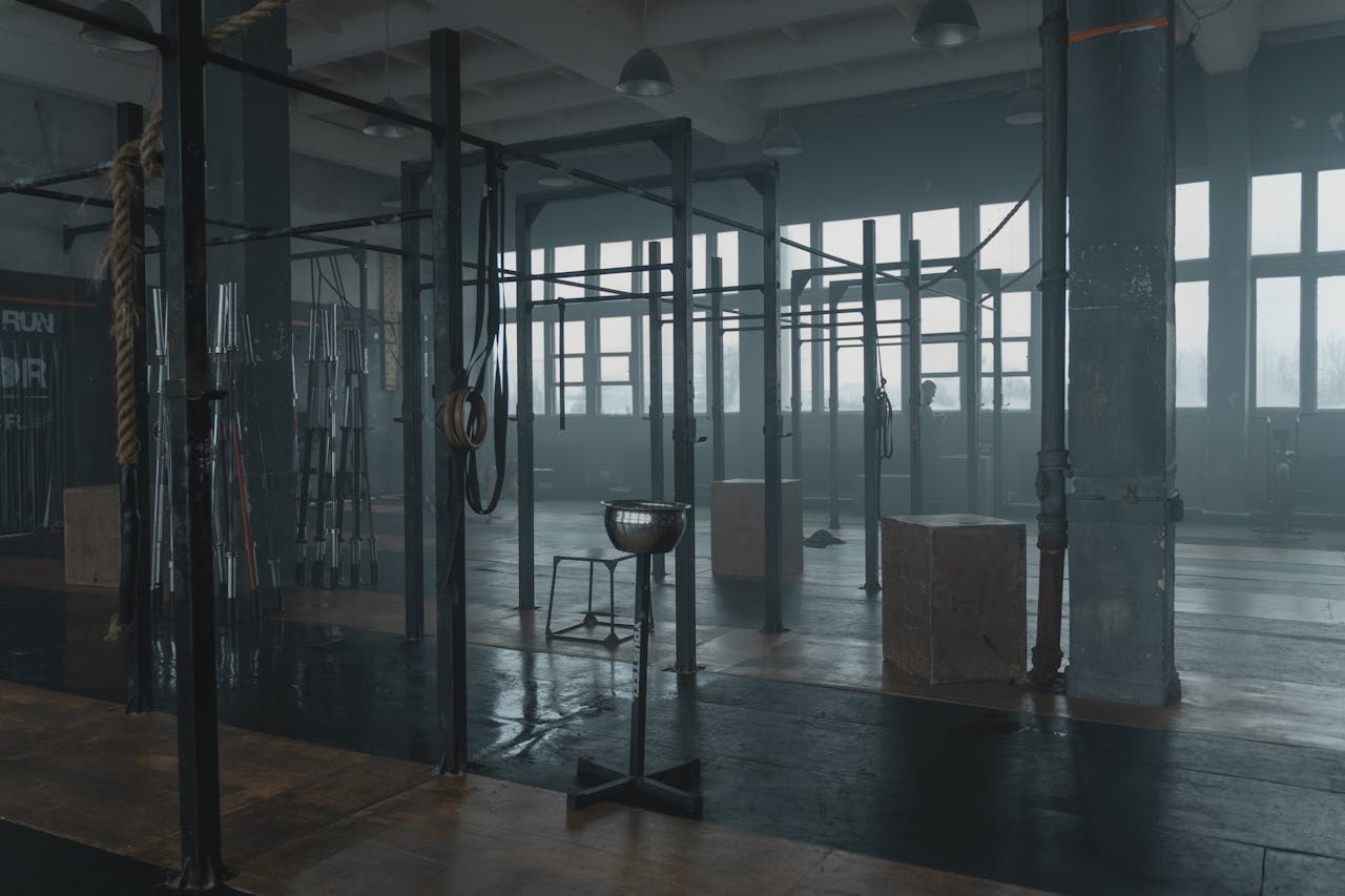 Moody gym interior featuring various workout equipment like pull-up bars and ropes in a spacious industrial setting.